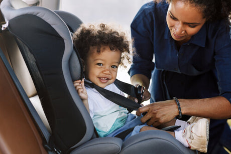 A Black woman securing a baby into a car seat 