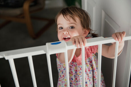 A little girl standing behind a safety gate