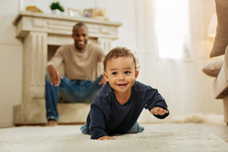 a baby crawling on the carpte infront of his dad